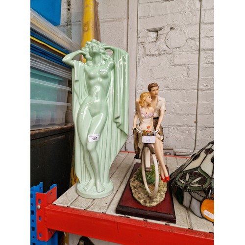 107 - Two pottery figures, lady and a couple on a bicycle mounted on a plinth