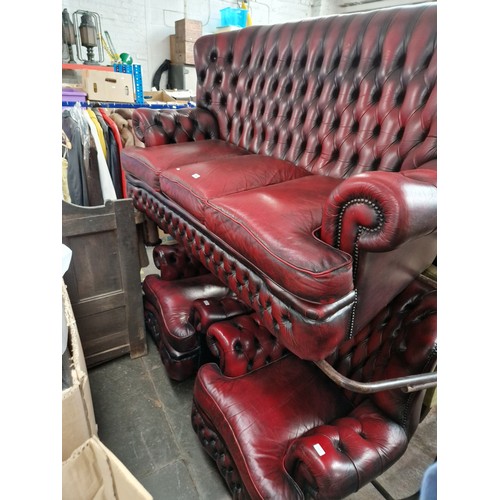 1096 - An oxblood red leather Chesterfield sofa and two matching armchairs.