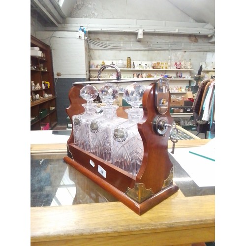 89 - A three bottle mahogany tantalus with cut glass decanters & hallmarked silver labels for whiskey, br... 