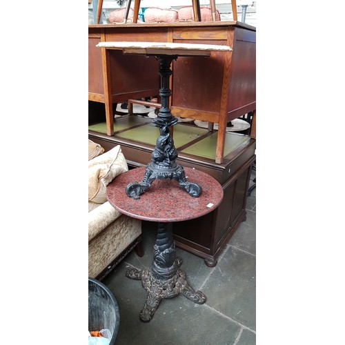 1009 - A pair of cast iron tables, one with marble top, the other with granite top, height 72cm & diameter ... 