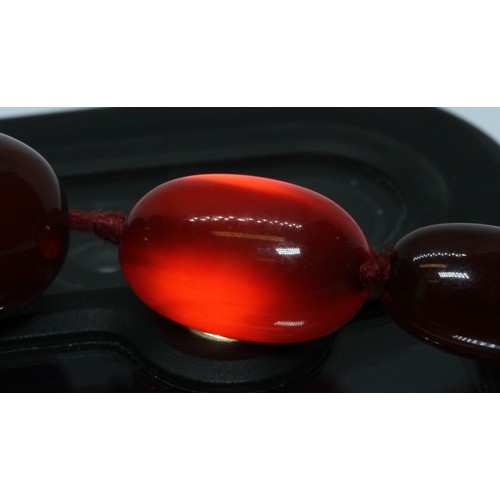 72 - A single strand graduated marbled cherry bakelite beads, the oval beads ranging in length from 13mm ... 