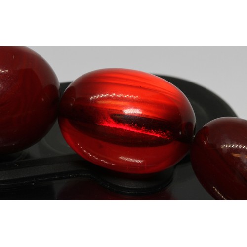 71 - A single strand of graduated marbled cherry bakelite beads, the oval shaped beads ranging in length ... 