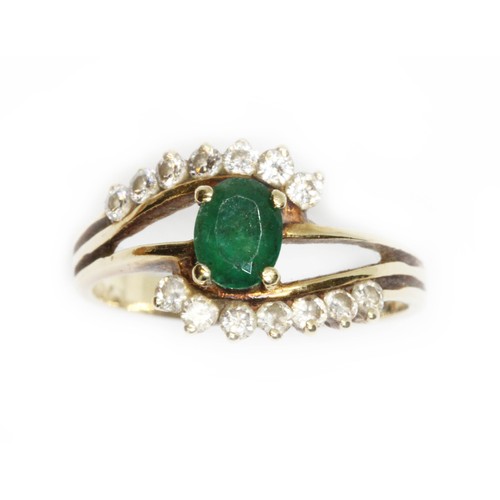 41 - An emerald and diamond cross over ring, the central oval faceted stone weighing approximately 0.44ct... 