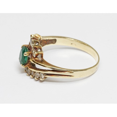 41 - An emerald and diamond cross over ring, the central oval faceted stone weighing approximately 0.44ct... 