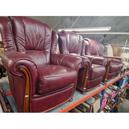 957 - An oxblood red leather two seater sofa together with two matching armchairs.