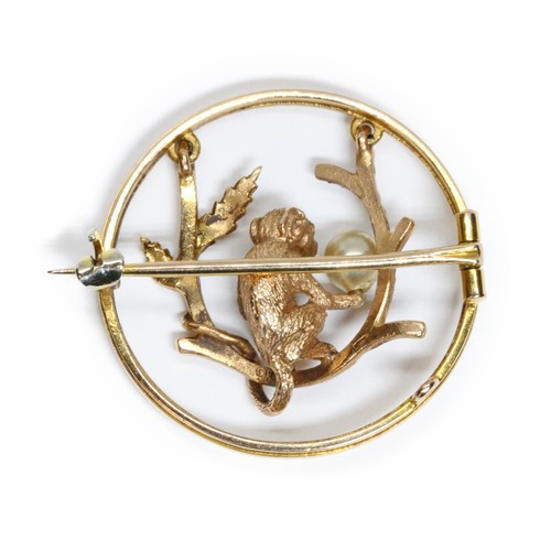 28 - A vintage swinging monkey brooch, the monkey modelled holding a pearl and sat on branch, within circ... 