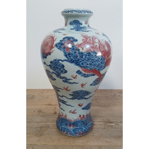 614 - A Chinese porcelain baluster vase decorated in red and blue underglaze depicting a dragon amongst cl...