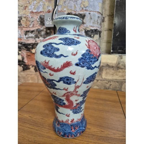 614 - A Chinese porcelain baluster vase decorated in red and blue underglaze depicting a dragon amongst cl... 