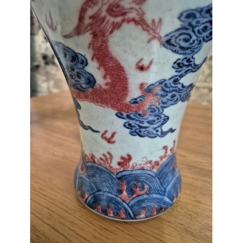 614 - A Chinese porcelain baluster vase decorated in red and blue underglaze depicting a dragon amongst cl... 