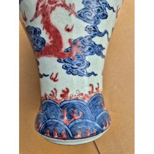 614 - A Chinese porcelain baluster vase decorated in red and blue underglaze depicting a dragon amongst cl... 