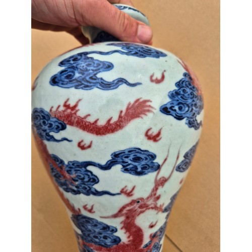 614 - A Chinese porcelain baluster vase decorated in red and blue underglaze depicting a dragon amongst cl... 
