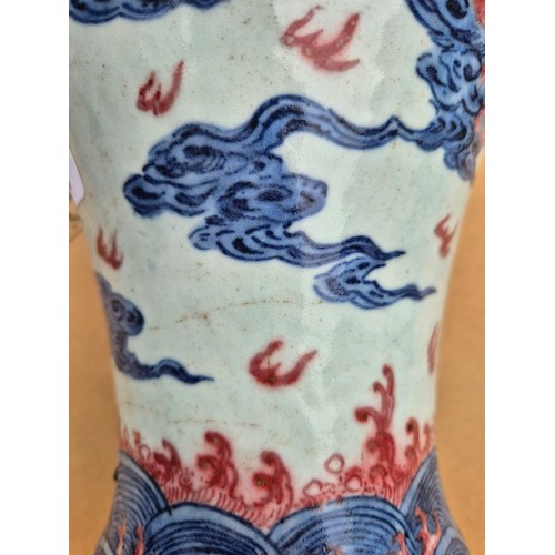 614 - A Chinese porcelain baluster vase decorated in red and blue underglaze depicting a dragon amongst cl... 
