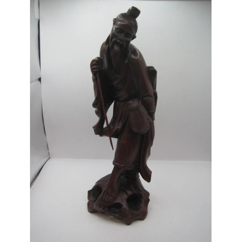 144 - Far Eastern carved red stained figure of man with staff and basket on a naturalistic base. Height 30... 