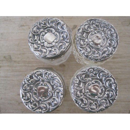 77 - 4 small glass dressing table pots with silver lids, the lids with repousse floral decor.