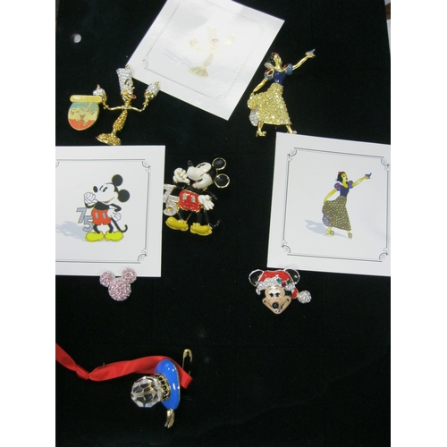 232 - A folder containing Walt Disney brooches and badges including a number produced by Swarovski, all in... 