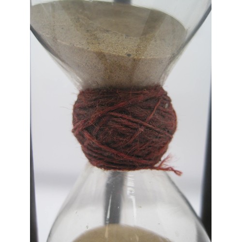 45 - A Victorian hand-blown hourglass in an ebony spindle frame. The glass is bound with red thread at th... 