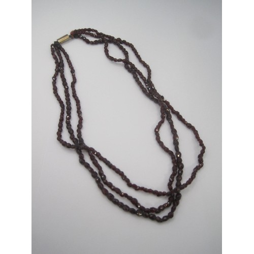 121 - A triple-strand faceted garnet bead necklace with yellow metal clasp