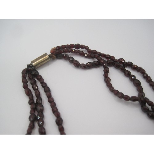 121 - A triple-strand faceted garnet bead necklace with yellow metal clasp