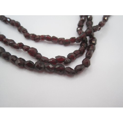 121 - A triple-strand faceted garnet bead necklace with yellow metal clasp