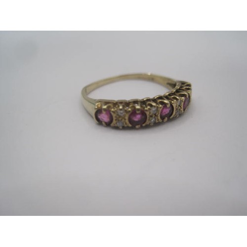 267 - A gold ruby and diamond dress ring. A row of five small rubies spaced by four pairs of very small di... 