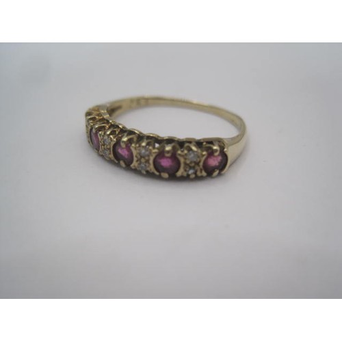 267 - A gold ruby and diamond dress ring. A row of five small rubies spaced by four pairs of very small di... 