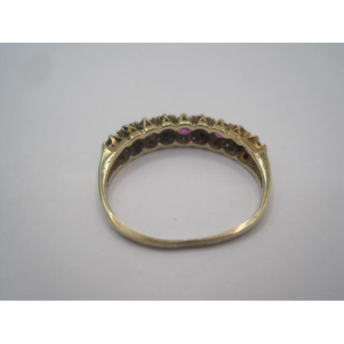 267 - A gold ruby and diamond dress ring. A row of five small rubies spaced by four pairs of very small di... 