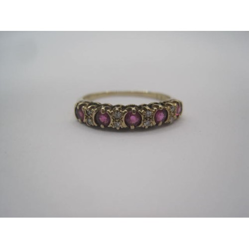 267 - A gold ruby and diamond dress ring. A row of five small rubies spaced by four pairs of very small di... 