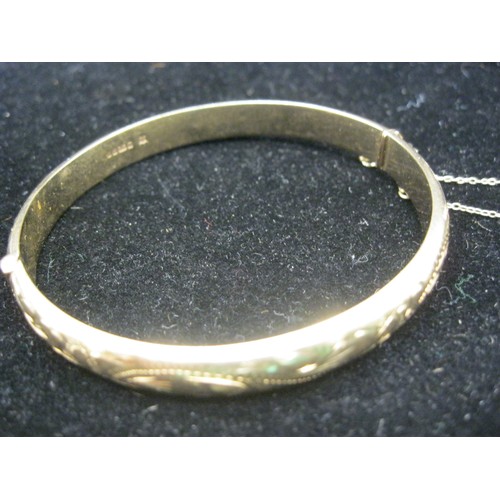 40 - A 9 carat gold bangle with foliate half engraving, safety chain. Gross weight approx. 9.8g