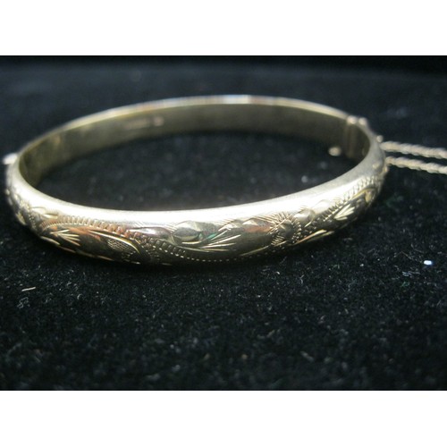 40 - A 9 carat gold bangle with foliate half engraving, safety chain. Gross weight approx. 9.8g