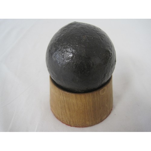 50 - A round shot iron cannon ball (approximately 7cms diameter) seated on a hardwood stand.