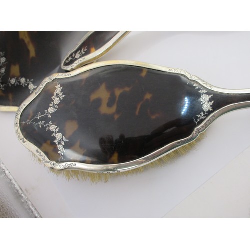 13 - An inlaid silver and tortoiseshell four-piece dressing table set comprising a clothes brush, two han... 