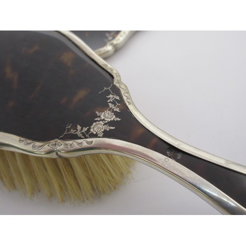 13 - An inlaid silver and tortoiseshell four-piece dressing table set comprising a clothes brush, two han... 