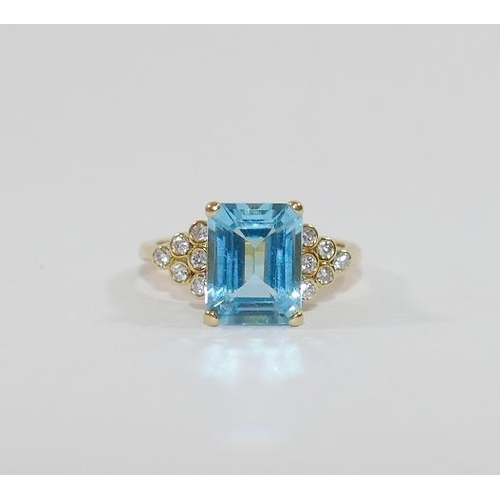 86 - An 18 carat gold blue topaz and diamond ring, the emerald cut topaz in four claw setting flanked on ... 