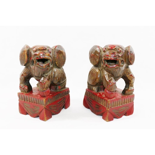 33 - A small pair of Chinese carved wooden temple dogs of foo, painted in red and gilt, on square bases, ... 