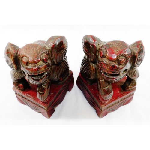 33 - A small pair of Chinese carved wooden temple dogs of foo, painted in red and gilt, on square bases, ... 