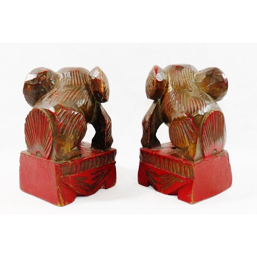 33 - A small pair of Chinese carved wooden temple dogs of foo, painted in red and gilt, on square bases, ... 