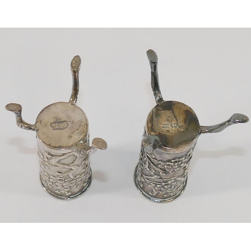 307 - A pair of small Chinese silver cylindrical vases, each raised on three legs and decorated with prunu... 