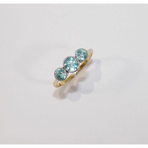 48 - A blue zircon three stone yellow metal ring, the graduated round mixed cut stones in white millegrai... 