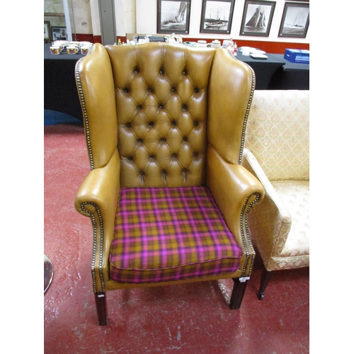 275 - A wing back library chair upholstered in brown coloured button back leather with applied studded dec... 