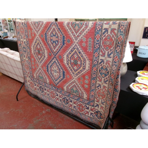 265 - An oriental floor rug on red and neutral coloured ground with geometric decoration