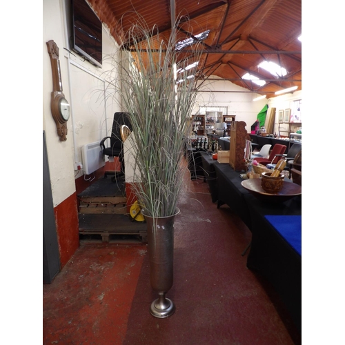 142 - A metallic vase with hand beaten decoration containing a spray of artificial grasses