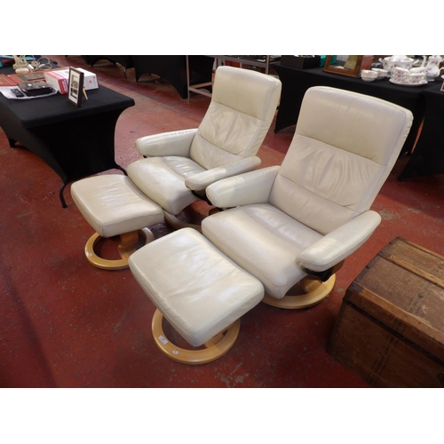 245 - A pair of Stressless revolving and reclining armchairs and foot stools upholstered in cream coloured... 