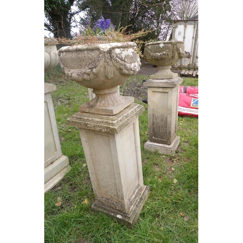 21 - A pair of reconstituted stone circular stemmed garden urns with swag decoration mounted upon a pair ... 