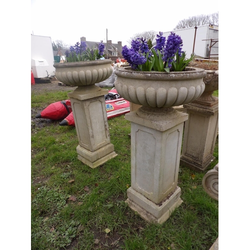 22 - A pair of reconstituted stone circular garden urns with fluted decoration on plinths