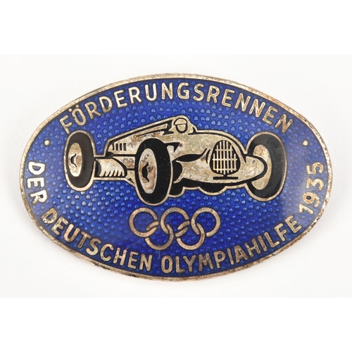 388 - A Third Reich pin back oval enamelled badge, depicting a racing car (Mercedes?) above the Olympic lo... 