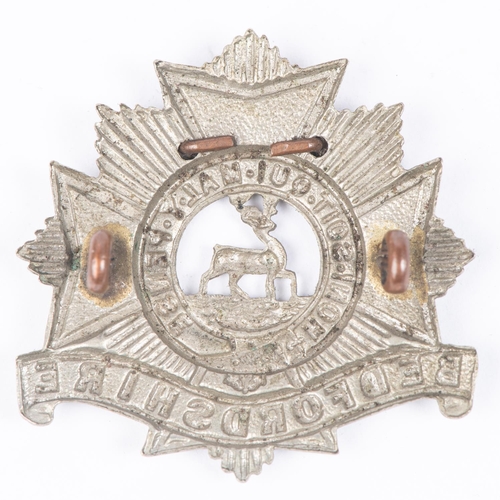 313 - A WM cap badge of the Bedfordshire Regiment, with additional wired on scroll 