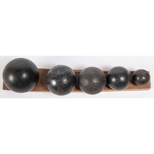 262 - Five small cast iron cannon/grapeshot balls, mounted on a wooden base in descending order of size, d... 