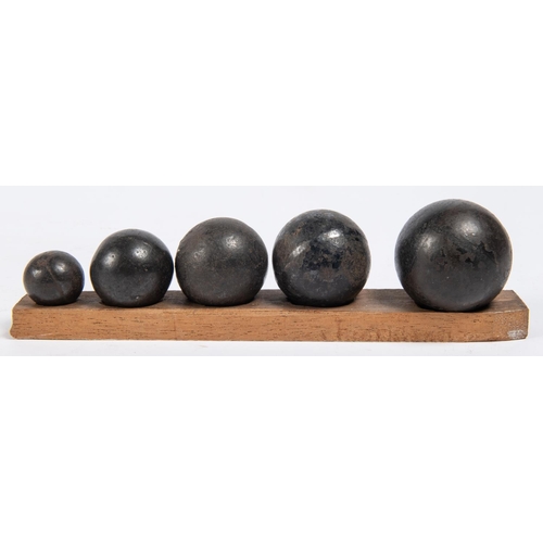 262 - Five small cast iron cannon/grapeshot balls, mounted on a wooden base in descending order of size, d... 