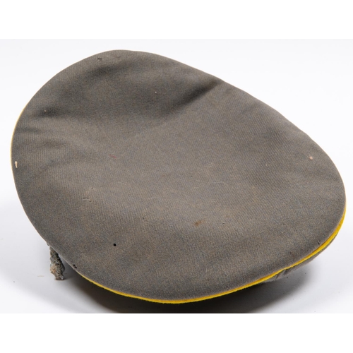 161 - A well made copy of a Third Reich cavalry officer's peaked cap, grey with yellow piping, alloy badge... 