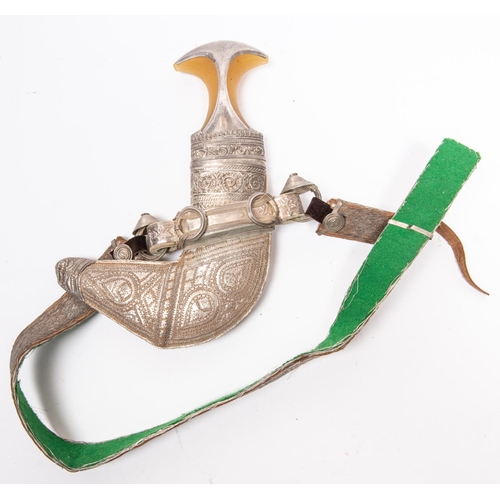 328 - An Arab jambiya with scabbard, embellished with silvered braid and white metal, on its braided belt.... 